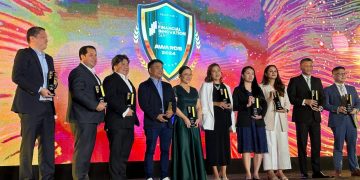 A group of people standing on a stage holding trophies Description automatically generated